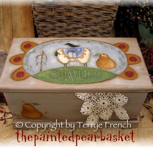 May include: A wooden box with a painted design of a sheep, a pear, and a bird. The box is painted in a rustic style with a light brown background and a blue sky. The words "Simplify" are painted on the box. The box is decorated with a crocheted doily.