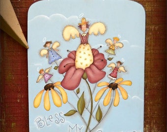 Op de afbeelding: Een blauw en wit geschilderd houten bord met de tekst "Bless My Blooms!" en een grillige illustratie van een bloem met engelen en wolken. Het bord is ontworpen door Terrye French en geschilderd door Sharon Bond.