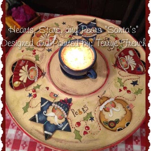 Könnte beinhalten: Ein Holztablett mit einem bemalten Design aus Herzen, Sternen und Birnen. Das Tablett verfügt über einen Kerzenhalter in der Mitte und den Text "Hearts, Stars, and Pears "Santa's" Designed and Painted by: Terrye French".