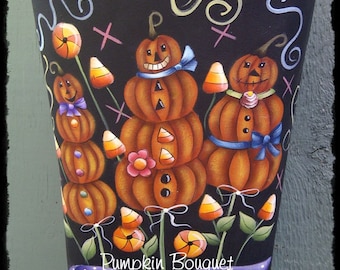 May include: A black metal container with a scalloped top, painted with a whimsical Halloween scene. Three stacked pumpkins with candy corn and a purple bow are surrounded by swirls and crosses. The text "Pumpkin Bouquet" is written on a purple ribbon at the bottom, with the words "Designed inspiration by Terrie French" and "Painted by Deb Antonick" below.