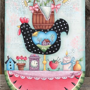 May include: A black and white polka dot chicken with a heart-shaped window in its chest. The window shows a small house with a red roof and a blue sky. The chicken is holding a basket of white daisies with pink bows. The chicken is standing on a watermelon slice with the words "Live Simply" written in pink letters. The words "Copyright Deb Antonick" and "www.paintingwithdeb.com" are written below the watermelon.