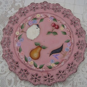 May include: A pink ceramic plate with a scalloped edge and a hand-painted design featuring a white sheep, a pear, a bird, and red cherries. The plate is decorated with a floral pattern and white dots.