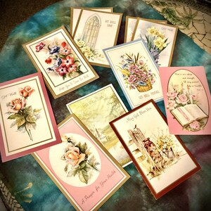 May include: A collection of vintage greeting cards with floral and religious themes. The cards feature illustrations of roses, bouquets, and church scenes, with text such as "Get Well" and "May God Bless You". The cards have gold borders and are arranged on a patterned surface.