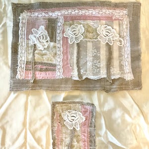 May include: Two rectangular fabric collages featuring layered beige corduroy, pink fabric strips, and white lace trim. The larger piece displays three white lace rose appliqués, while the smaller piece features one white lace rose appliqué.
