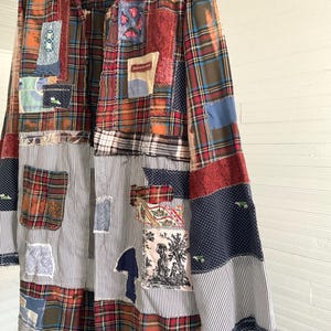 May include: A long-sleeved button-down shirt featuring a patchwork design of various fabrics, including red, green, and blue plaid, black and white pinstripes, navy blue polka dots, and a square patch with a black and white toile print illustration.