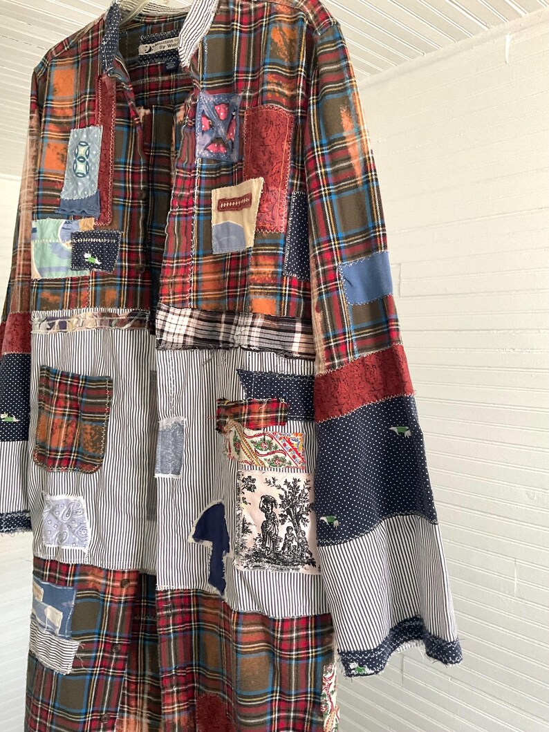 May include: A long-sleeved button-down shirt featuring a patchwork design of various fabrics, including red, green, and blue plaid, black and white pinstripes, navy blue polka dots, and a square patch with a black and white toile print illustration.