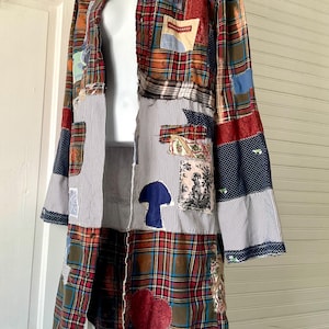 May include: A long-sleeved button-down shirt featuring a patchwork design of red, green, and blue plaid fabric combined with blue and white pinstriped panels. The garment includes various fabric patches, a blue mushroom shape, and a red heart.