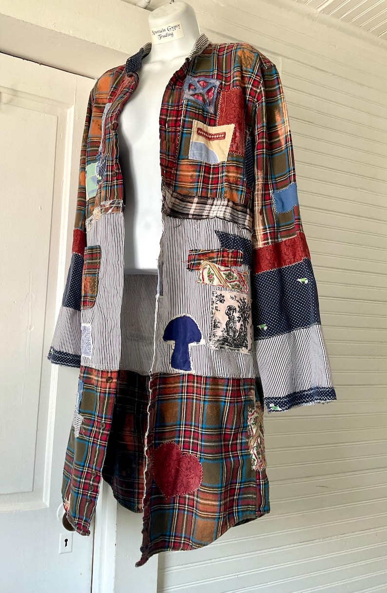 May include: A long-sleeved button-down shirt featuring a patchwork design of red, green, and blue plaid fabric combined with blue and white pinstriped panels. The garment includes various fabric patches, a blue mushroom shape, and a red heart.