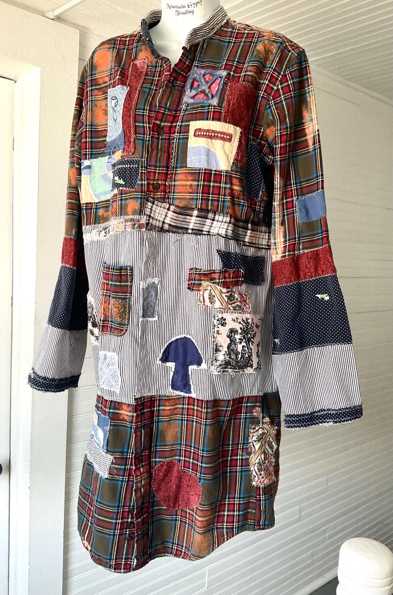 May include: A long-sleeved shirt featuring a patchwork design of red, blue, and green plaid fabric combined with black and white pinstriped panels. The garment includes various fabric appliqu&eacute;s, including a blue mushroom shape and a toile print.
