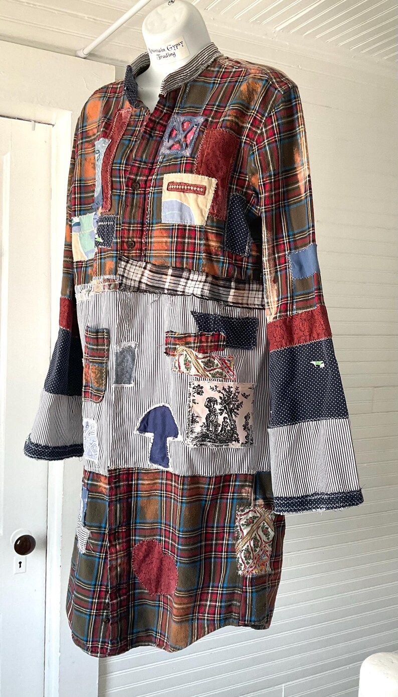 May include: A long-sleeved shirt featuring a patchwork design of red, green, and blue plaid fabric combined with sections of black and white pinstriped fabric. The garment includes various fabric patches in floral, polka dot, and toile patterns.