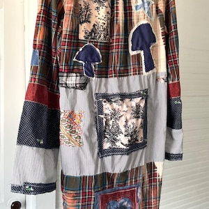 May include: A long-sleeve button-down shirt featuring a patchwork design of various fabrics including red and green plaid, blue and white pinstripes, and floral prints. The shirt includes appliqued shapes like mushrooms and a heart.