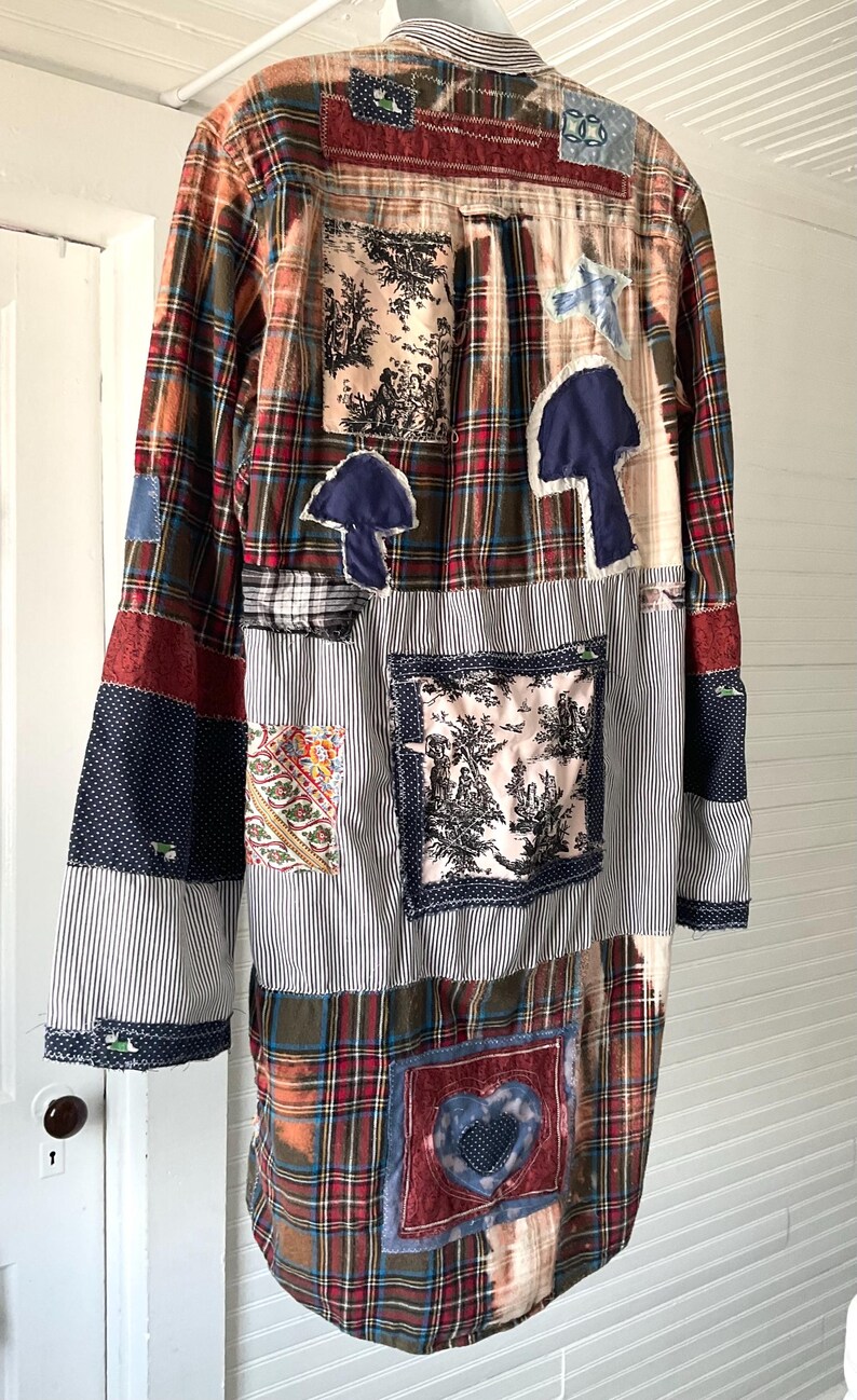 May include: A long-sleeve button-down shirt featuring a patchwork design of various fabrics including red and green plaid, blue and white pinstripes, and floral prints. The shirt includes appliqued shapes like mushrooms and a heart.