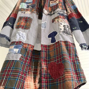 May include: A long-sleeved button-down shirt featuring a patchwork design of various plaid, striped, and solid fabrics in red, blue, brown, and white. The garment includes decorative appliqu&eacute;s such as a dark red heart and a blue mushroom shape.