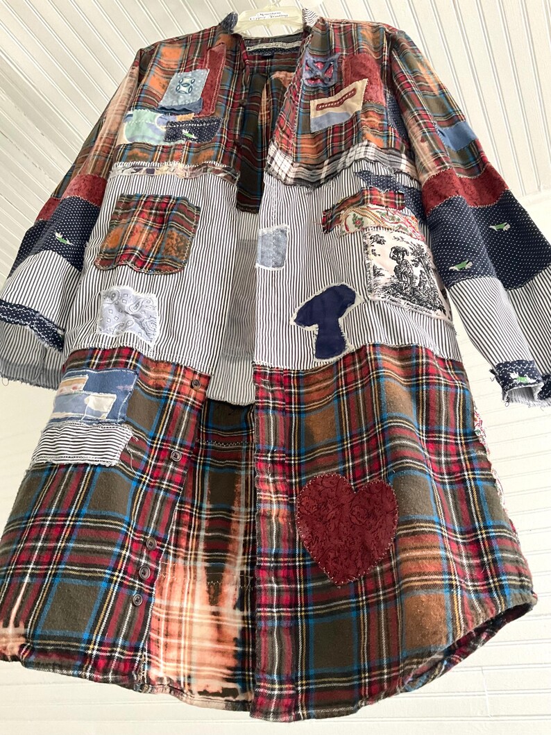 May include: A long-sleeved button-down shirt featuring a patchwork design of various plaid, striped, and solid fabrics in red, blue, brown, and white. The garment includes decorative appliqu&eacute;s such as a dark red heart and a blue mushroom shape.