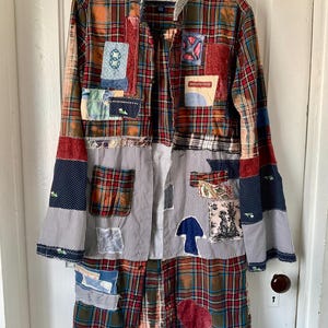 May include: A long-sleeved button-down shirt featuring a patchwork design of red, green, and blue plaid fabric mixed with white and black pinstriped panels. The garment is adorned with various fabric patches, including a blue mushroom and a dog.