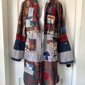 May include: A long-sleeved button-down shirt featuring a patchwork design of red, green, and blue plaid fabric combined with black and white pinstriped panels. The garment is decorated with various fabric patches, including a blue mushroom shape.