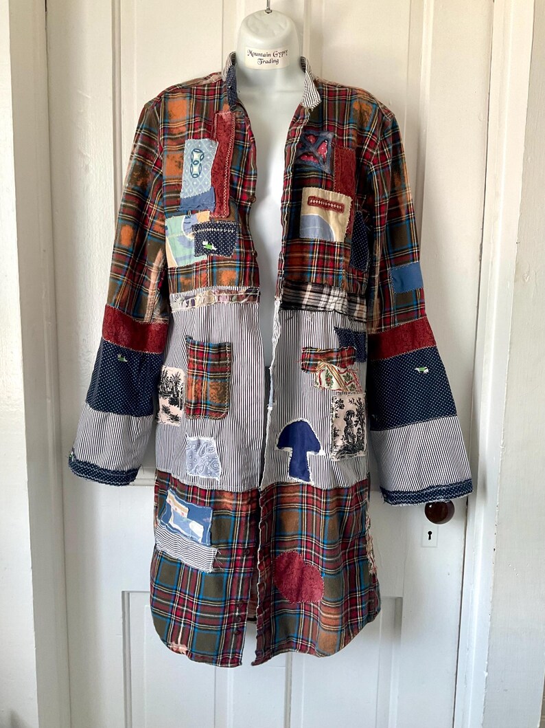 May include: A long-sleeved button-down shirt featuring a patchwork design of red, green, and blue plaid fabric combined with black and white pinstriped panels. The garment is decorated with various fabric patches, including a blue mushroom shape.