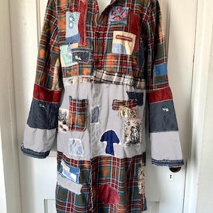 May include: A long-sleeved button-down shirt featuring a patchwork design of red, green, and blue plaid fabric combined with black and white pinstriped panels. The garment is decorated with various fabric patches, including a blue mushroom shape.