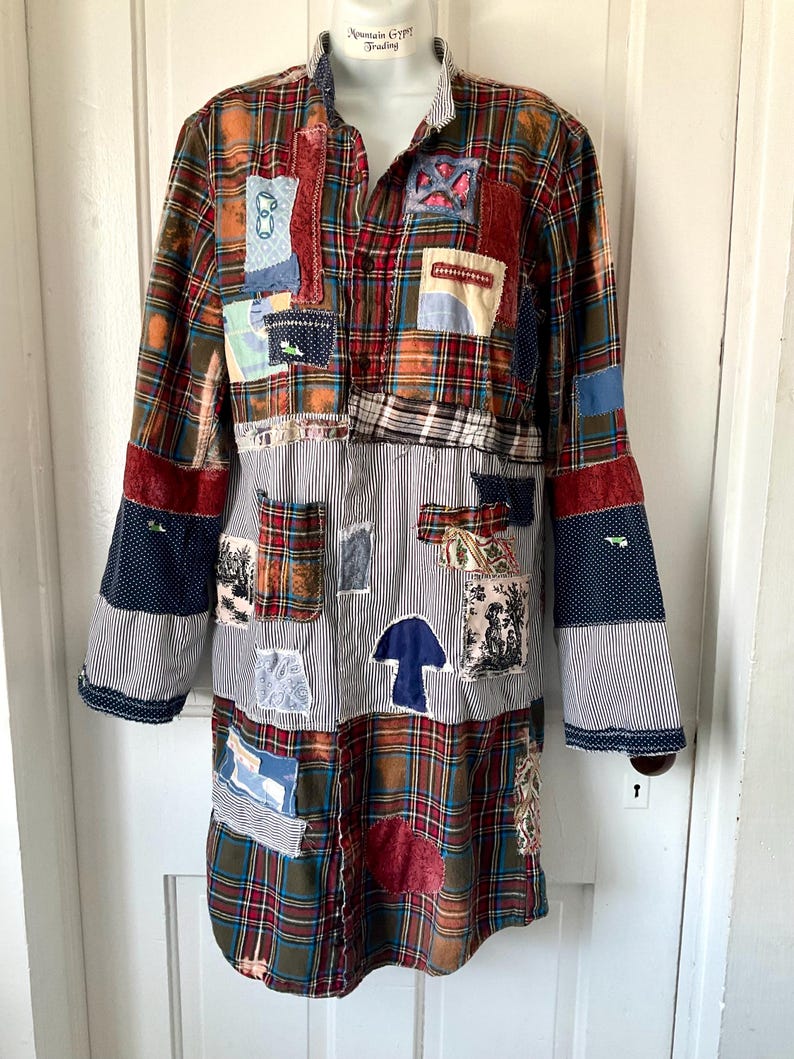 May include: A long-sleeved button-down shirt featuring a patchwork design of red, green, and blue plaid fabric combined with black and white pinstriped panels. The garment is decorated with various fabric patches, including a blue mushroom shape.