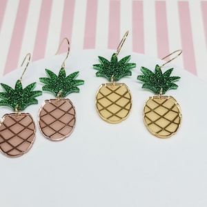 May include: A pair of gold and rose gold pineapple earrings with green glitter pineapple tops.