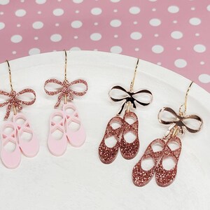 Puede incluir: Un par de pendientes de bailarina rosa con lazos dorados y un par de pendientes de bailarina de oro rosa con lazos dorados.