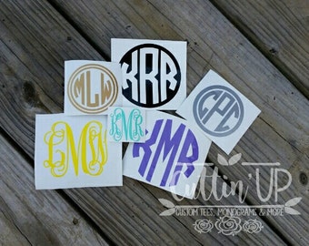May include: A collection of monogram decals in various colors, including gold, black, yellow, teal, purple, and gray. Each decal features a unique three-letter monogram design within a circle or oval shape. The image also includes the text "Cuttin' Up" with the tagline "Custom Tees, Monograms & More."