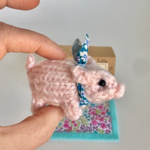 Un cerdito bebé muy lindo tejido a mano en una caja con una manta.