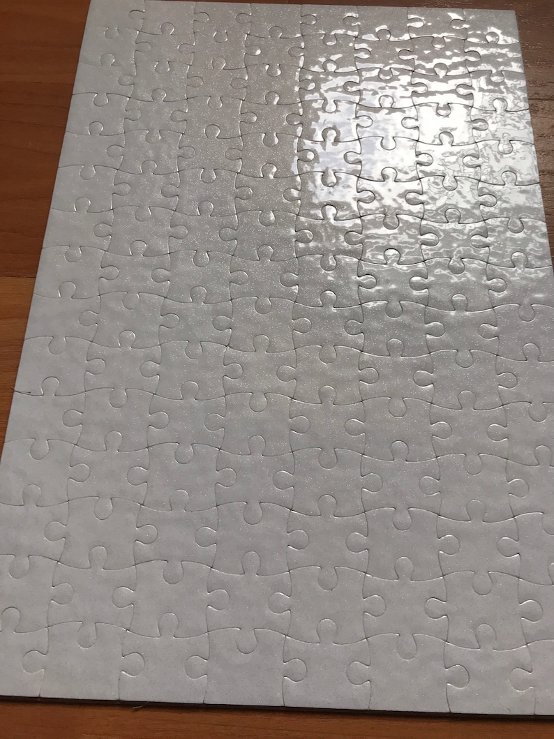 May include: A completed white jigsaw puzzle with interlocking pieces. The puzzle is rectangular and appears to be on a wooden surface. The pieces have a slight sheen, reflecting light.