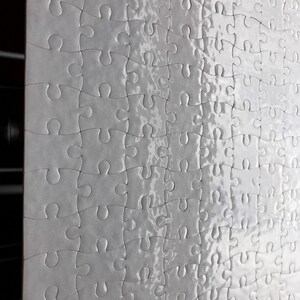 May include: A partially assembled white jigsaw puzzle. The puzzle pieces are interlocking, with a glossy, reflective surface. The image shows a close-up of the puzzle, highlighting the individual pieces and their unique shapes. The puzzle is a leisure activity.