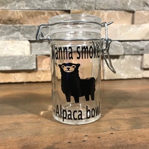 May include: A clear glass jar with a silver lid and a black and white sticker that says "Wanna smoke Alpaca bowl". The sticker features a cartoon alpaca.
