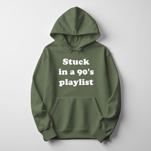 May include: Olive green hoodie with a front pocket and drawstring. The white text on the front reads "Stuck in a 90's playlist". The hooded sweatshirt is a casual style.