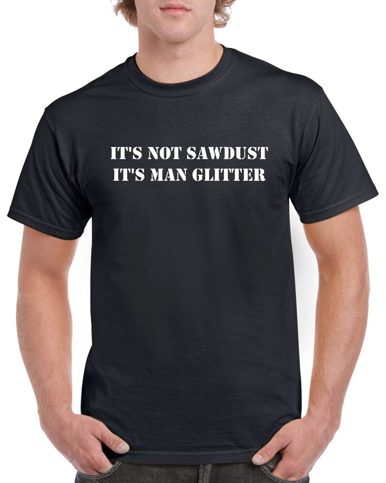May include: Black crew neck t-shirt with the white text "IT'S NOT SAWDUST IT'S MAN GLITTER". The shirt is made of a soft material and has short sleeves. The person is wearing the shirt.