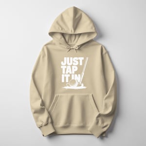 Puede incluir: Una sudadera con capucha de color beige con un bolsillo delantero y una capucha con cord&oacute;n. La parte delantera presenta el texto blanco "JUST TAP IT IN" con un gr&aacute;fico de pelota y palo de golf. La sudadera est&aacute; hecha de un material suave.