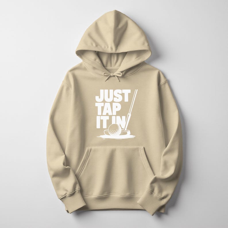 Puede incluir: Una sudadera con capucha de color beige con un bolsillo delantero y una capucha con cord&oacute;n. La parte delantera presenta el texto blanco "JUST TAP IT IN" con un gr&aacute;fico de pelota y palo de golf. La sudadera est&aacute; hecha de un material suave.