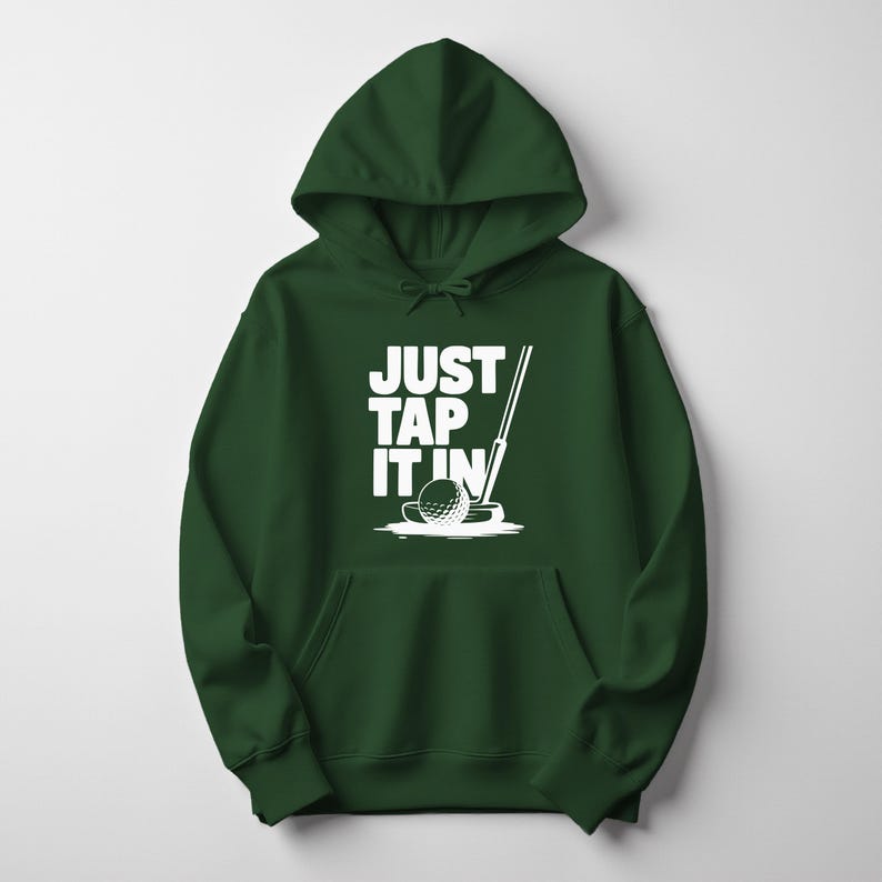 Puede incluir: Una sudadera con capucha verde oscuro con un bolsillo delantero. La sudadera presenta un gr&aacute;fico blanco de una pelota de golf, un palo de golf y el texto "JUST TAP IT IN". El dise&ntilde;o est&aacute; centrado en la parte delantera de la prenda.