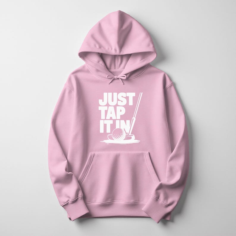 Puede incluir: Sudadera con capucha rosa claro con bolsillo delantero y capucha con cord&oacute;n. La parte delantera muestra el texto blanco "JUST TAP IT IN" y un gr&aacute;fico de una pelota de golf y un palo.