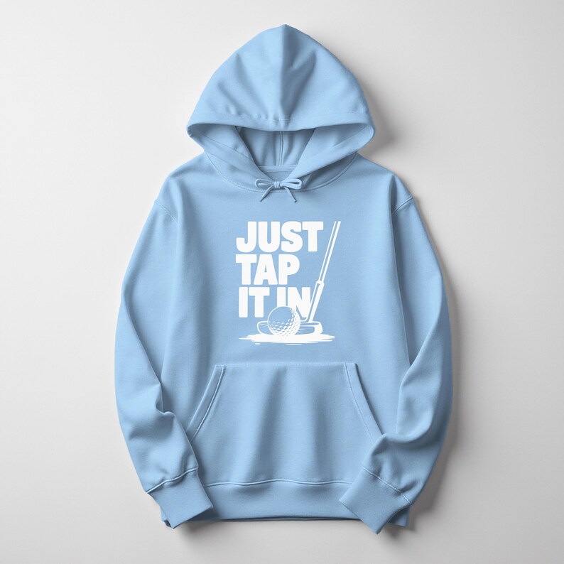 Puede incluir: Sudadera con capucha azul claro con bolsillo delantero y capucha con cord&oacute;n. El frente presenta el texto blanco "JUST TAP IT IN" con un gr&aacute;fico de pelota y palo de golf. Prenda casual y c&oacute;moda.