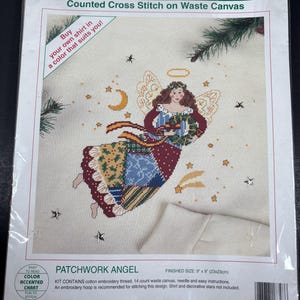 May include: A Sunset counted cross-stitch kit featuring a Patchwork Angel design. The kit includes cotton embroidery thread, a 14-count waste canvas, and easy instructions. Finished size is 9 x 9 inches. The packaging includes text that says "Buy your own shirt in a color that suits you!"