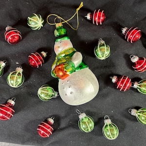 May include: A collection of vintage Christmas ornaments, including red and green glass baubles and a snowman figure. The ornaments have a festive appearance, with a variety of shapes and designs, perfect for holiday decorating.