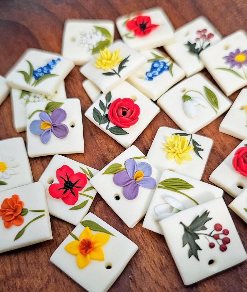 May include: A collection of square, off-white ceramic tiles, each featuring a raised, three-dimensional floral design in various colors including red, yellow, purple, orange, and blue, with a small circular hole punched near one corner.
