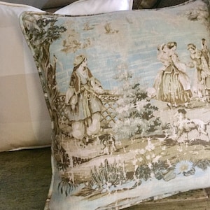 May include: A decorative pillow with a light blue background and a brown and white patterned design. The pattern features a pastoral scene with figures in period clothing and a dog.