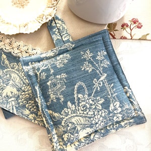 May include: Two blue and white fabric pot holders with a floral pattern. The pot holders have a loop handle and are quilted.