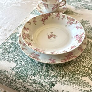May include: A set of white porcelain dishes with a floral pattern. The dishes are on a white tablecloth with a green and white pattern.