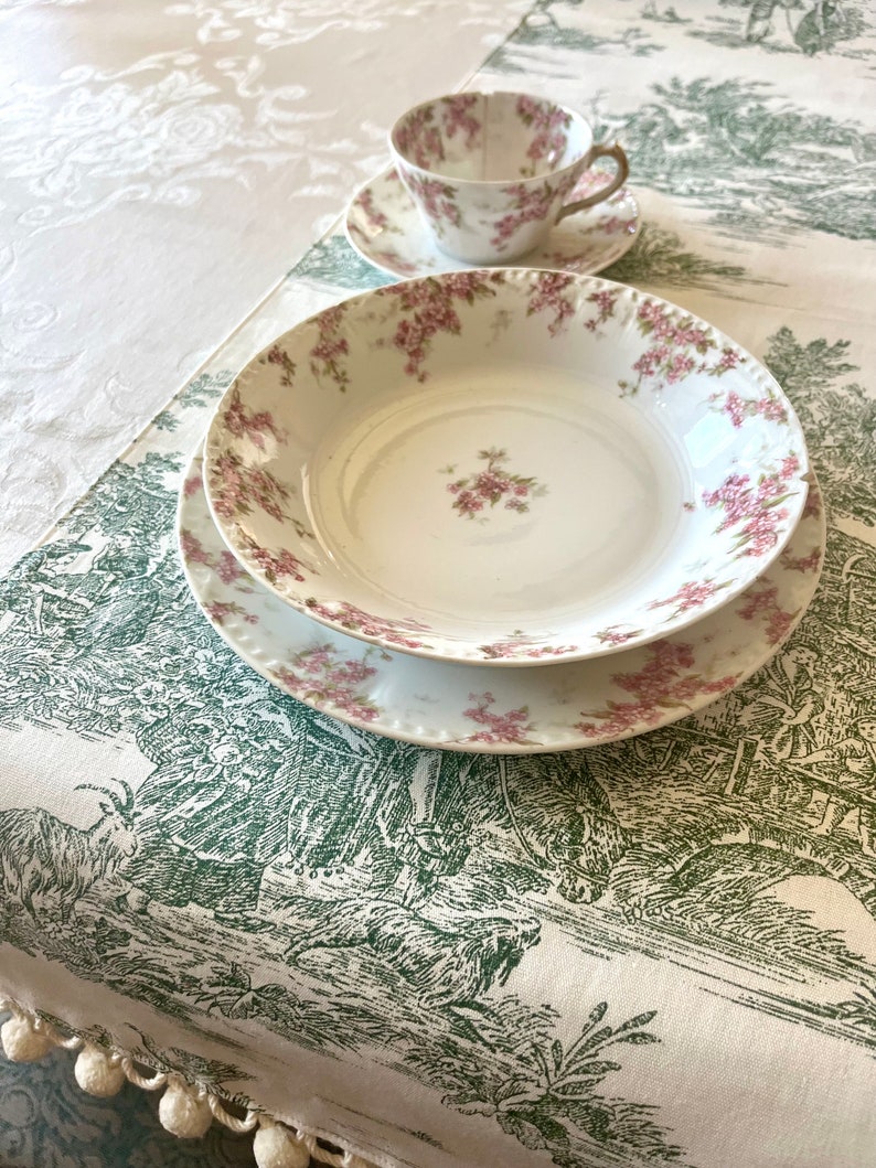 May include: A set of white porcelain dishes with a floral pattern. The dishes are on a white tablecloth with a green and white pattern.