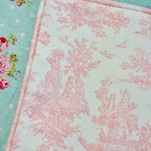 May include: A close-up of a pink and white fabric with a toile pattern. The pattern features a repeating design of trees, flowers, and birds. French Country Cottage decor.