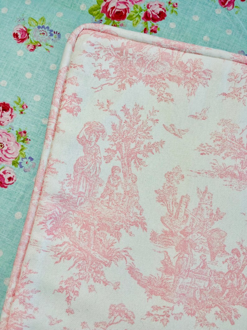 May include: A close-up of a pink and white fabric with a toile pattern. The pattern features a repeating design of trees, flowers, and birds. French Country Cottage decor.
