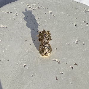 May include: A gold pineapple figurine on a white textured surface.