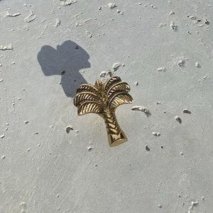 May include: A gold palm tree shaped door knob or pull. The palm tree is detailed with individual fronds and a textured trunk. The palm tree is on a white textured surface.