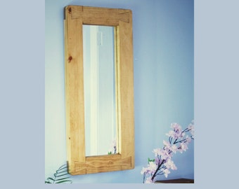 May include: A rectangular wall mirror featuring a light-toned natural wood frame with visible grain and distinct dovetail joinery at each corner. The mirror glass is clear and reflective, set within the thick, sturdy wooden border.