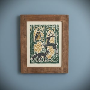 May include: A framed art print featuring a forest scene with an owl, deer, and fox. The print has a green, gold, and black color scheme. The frame is made of wood and has a natural finish. The artwork is mounted on a cream-colored background.